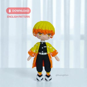 Może przedstawiać: Ręcznie robiona szydełkowa lalka postaci z żółtymi i pomarańczowymi włosami, w żółto-pomarańczowym płaszczu we wzory, czarnych spodniach i biało-czarnych butach. Widoczny jest tekst "DOWNLOAD ENGLISH PATTERN".