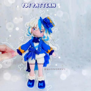 Puede incluir: Muñeca de crochet con cabello blanco, un sombrero azul y dorado, una chaqueta azul, una camisa blanca, un lazo azul, pantalones cortos blancos y zapatos azules. La muñeca está de pie sobre un fondo blanco con corazones dibujados a su alrededor. El texto "PDF PATTERN" está en la parte superior de la imagen.