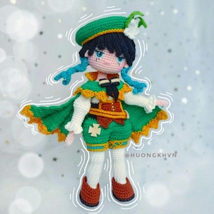 Peut inclure: Poupée au crochet faite à la main représentant un personnage portant un béret vert, une cape et un short avec une chemise blanche. La poupée a des cheveux et des yeux bleus, et des chaussures marron. La tenue de la poupée a des accents jaunes et orange. La poupée est un personnage du jeu Genshin Impact.