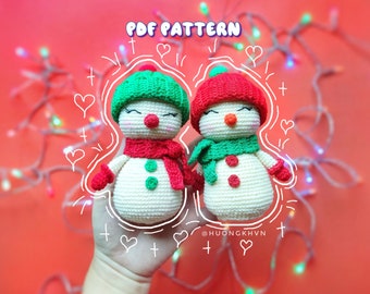 May include: Two crocheted snowman ornaments with red and green hats, scarves, and buttons. The snowmen are holding hands and are surrounded by hearts and plus signs. The text "PDF PATTERN" and "@HUONGKHVN" are also visible.