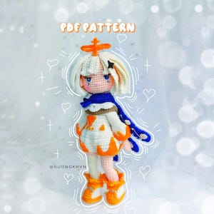以下が含まれることがあります： 白い糸で編まれた、オレンジ色のアクセントと青いスカーフをつけた、編みぐるみ人形。人形は頭に星をつけており、オレンジ色の炎がついた白いドレスを着ています。人形はハートとプラス記号で囲まれています。