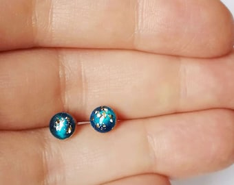 May include: A pair of small, round stud earrings with a dark blue background and gold flecks.