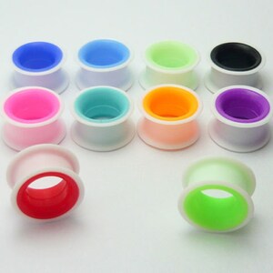 May include: Assortment of colourful silicone ear gauges with white outer rings. The gauges come in a variety of colours, including pink, blue, green, orange, and purple.