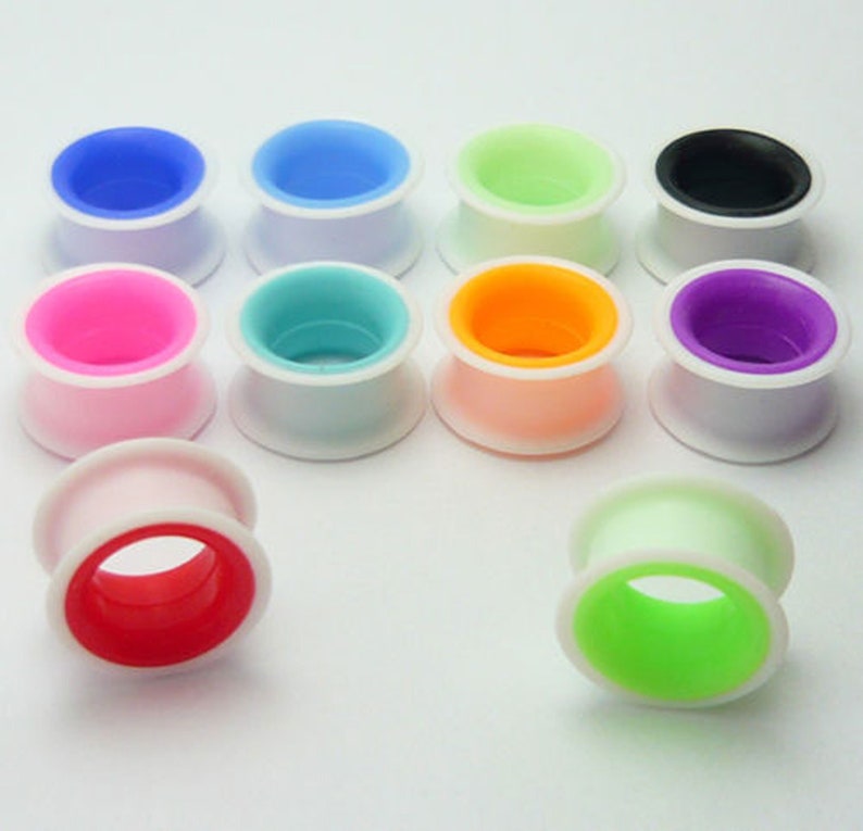 May include: Assortment of colourful silicone ear gauges with white outer rings. The gauges come in a variety of colours, including pink, blue, green, orange, and purple.
