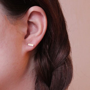 Könnte beinhalten: Nahaufnahme eines Ohrs mit einem kleinen, goldenen Stab-Ohrring. Der Ohrring ist schlicht und minimalistisch und ein beliebter Stil für den Alltag.