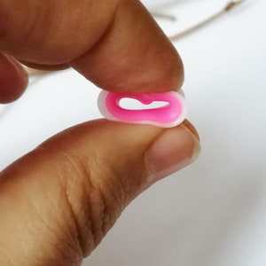 May include: A pink and white plastic bead with a heart-shaped hole in the centre.
