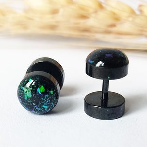Peut inclure: Une paire de jauges d'oreille en acier inoxydable noir avec un design de paillettes noires et vertes. Les jauges sont un type de bijoux de corps populaire.