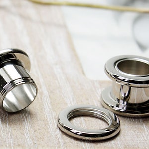 Puede incluir: Dos expansores de oreja de metal plateado, uno con un diámetro más grande que el otro, y un anillo de metal plateado más pequeño. Los expansores están diseñados para lóbulos de oreja estirados.