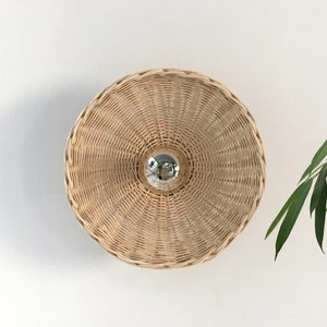 May include: A round, woven wicker light fixture against a white background. The light fixture is a natural, light brown colour and has a circular shape.