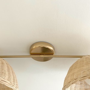 May include: A gold metal light fixture with two woven wicker shades. The fixture has a round base and a straight bar connecting the two shades.