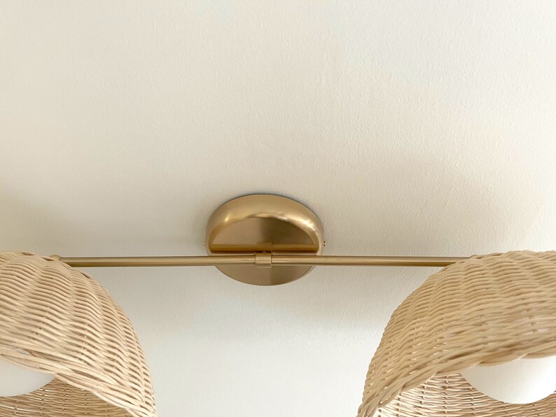 May include: A gold metal light fixture with two woven wicker shades. The fixture has a round base and a straight bar connecting the two shades.