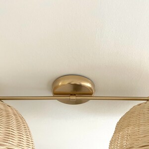 May include: A gold ceiling light fixture with two woven wicker shades. The fixture has a single arm that extends from the center.