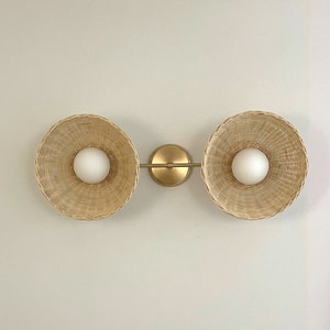 May include: A gold wall sconce with two woven wicker shades and white globe light bulbs.