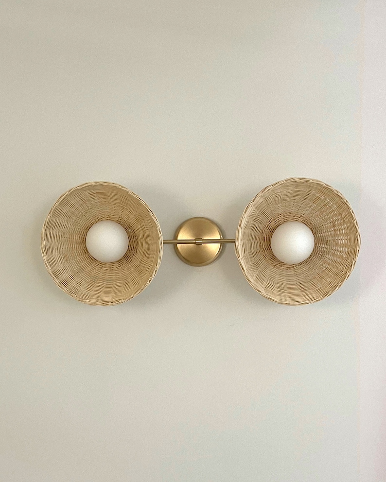 May include: A gold wall sconce with two woven wicker shades and white globe light bulbs.