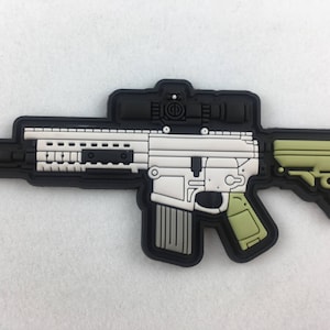 Könnte beinhalten: Schwarz-weißes Gewehr-Patch mit grünem Schaft und Zielfernrohr. Das Gewehr ist schwarz umrandet und hat einen weißen Innenraum.