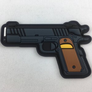 Può includere: Un cerotto di plastica nero e marrone che raffigura una pistola con un dettaglio giallo sull'impugnatura.