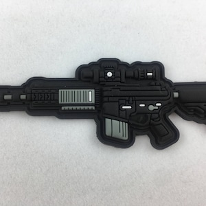May include: Black and gray tactical rifle patch with a scope and a silver detail on the barrel.