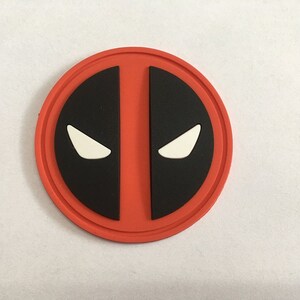 Puede incluir: Pegatina redonda roja y negra con un diseño de máscara de Deadpool blanco.