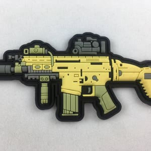 Peut inclure: Un patch de fusil tactique jaune et noir avec une lunette noire et grise et une poignée noire et grise.