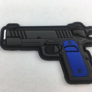 Può includere: Toppa per pistola nera e blu con superficie testurizzata. La pistola ha un'impugnatura blu e una canna argentata.