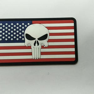 May include: A black and white embroidered patch with a skull and crossbones design on a red, white, and blue American flag background.