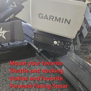 Puede incluir: Un buscador de peces Garmin blanco con el texto "GARMIN" en gris. El buscador de peces est&aacute; montado sobre una base negra con botones y una peque&ntilde;a pantalla. La imagen tambi&eacute;n incluye texto que dice "Monte su estaci&oacute;n de acoplamiento y sonar de avance favorito en cualquier lugar a lo largo de su riel Targas Versatrack."