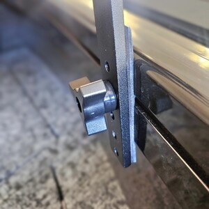 Puede incluir: Primer plano de un sistema de rieles de caja de cami&oacute;n de metal negro con una perilla de pl&aacute;stico negro. El sistema est&aacute; dise&ntilde;ado para asegurar art&iacute;culos en la caja de un cami&oacute;n.