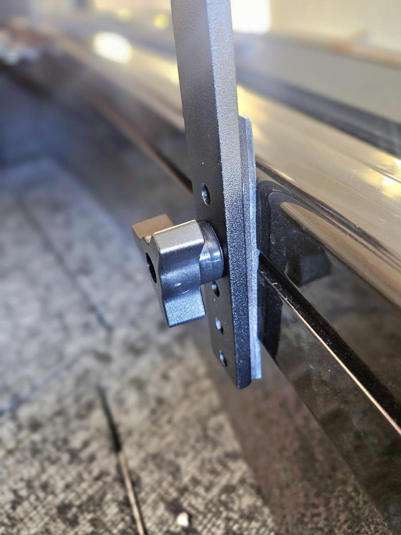 Puede incluir: Primer plano de un sistema de rieles de caja de cami&oacute;n de metal negro con una perilla de pl&aacute;stico negro. El sistema est&aacute; dise&ntilde;ado para asegurar art&iacute;culos en la caja de un cami&oacute;n.