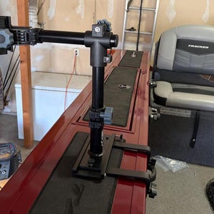 Puede incluir: Un soporte de barco ajustable negro y gris con un brazo horizontal y un soporte vertical. El soporte est&aacute; fijado a una superficie de barco roja. El soporte tiene varias perillas ajustables. Un asiento gris est&aacute; en el fondo.