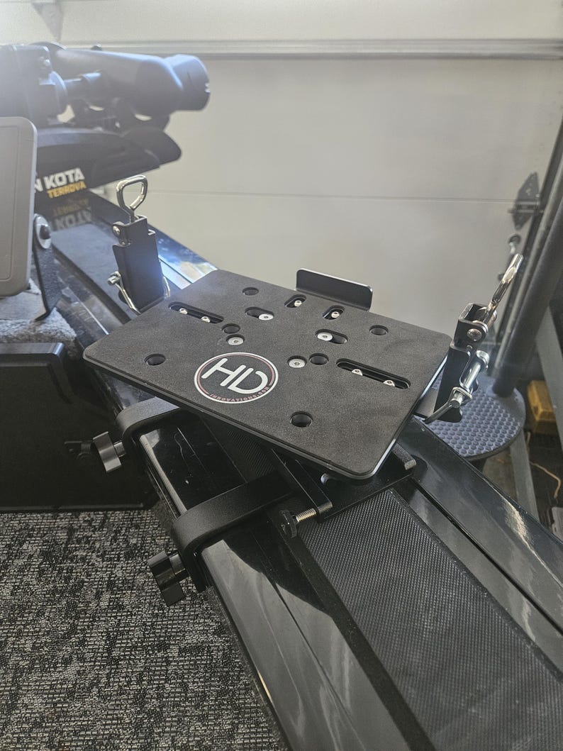 Puede incluir: Una placa de montaje de metal negro con las letras "HD" en un c&iacute;rculo blanco est&aacute; unida a un componente de barco negro. La placa tiene m&uacute;ltiples agujeros y herrajes de montaje. La imagen muestra un primer plano del sistema de montaje.