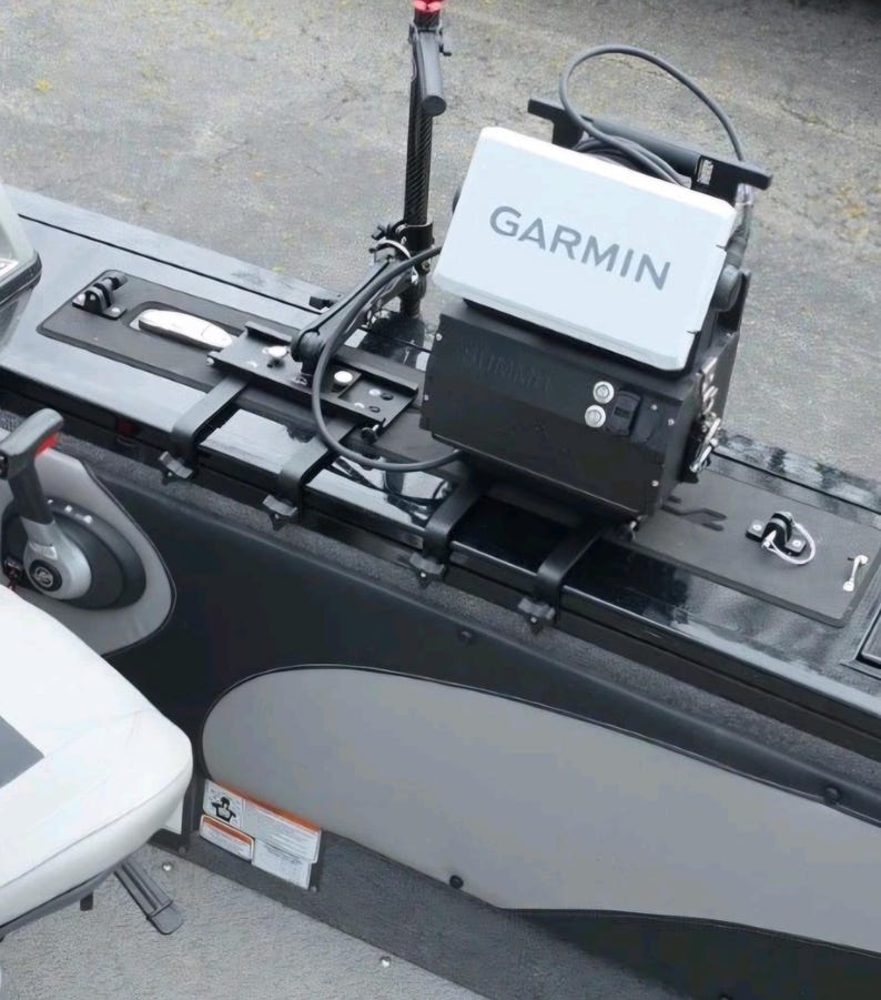 Puede incluir: Un buscador de peces Garmin y equipos relacionados est&aacute;n montados en un barco. El buscador de peces es blanco con el logotipo de Garmin. El barco tiene detalles en negro y gris, con un asiento blanco visible.