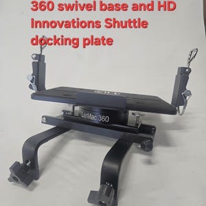 Puede incluir: Una placa de acoplamiento de metal negro con una base giratoria. La placa tiene una parte superior rectangular y est&aacute; soportada por patas curvas con perillas ajustables. El texto en la placa dice "LarMac 360". La imagen tambi&eacute;n incluye texto.
