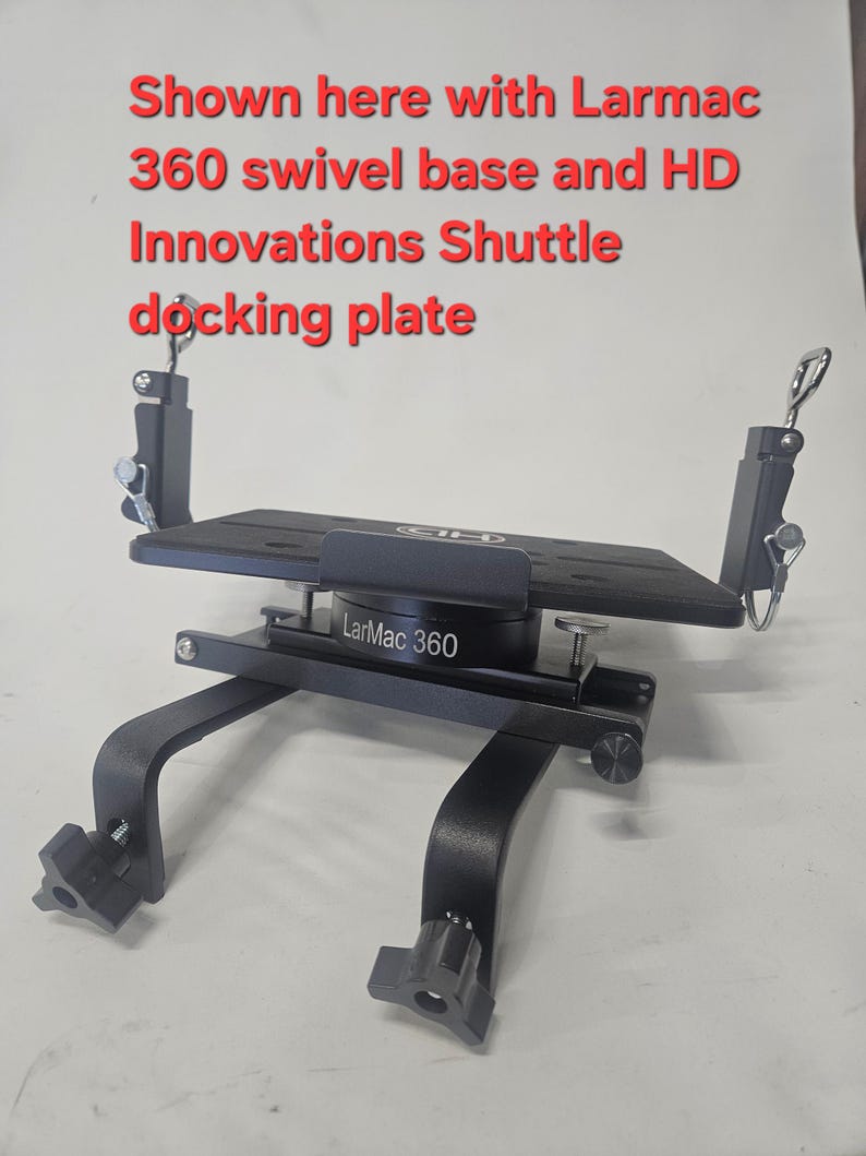 Puede incluir: Una placa de acoplamiento de metal negro con una base giratoria. La placa tiene una parte superior rectangular y est&aacute; soportada por patas curvas con perillas ajustables. El texto en la placa dice "LarMac 360". La imagen tambi&eacute;n incluye texto.