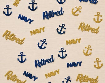 May include: A collection of glittery confetti pieces in gold and dark blue. The shapes include anchors and the words "Retired" and "NAVY" in various orientations. The pieces have a textured, sparkling finish and are scattered across the frame.