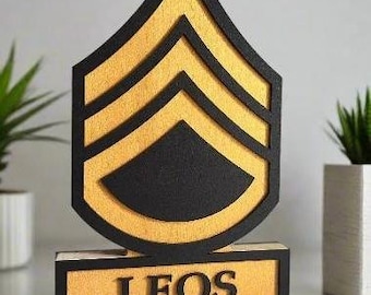 May include: A wooden plaque with a black and gold chevron design and the name "LEOS" in black lettering.