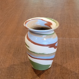 May include: A small, white ceramic vase with a swirl pattern in shades of green, blue, brown, and beige.