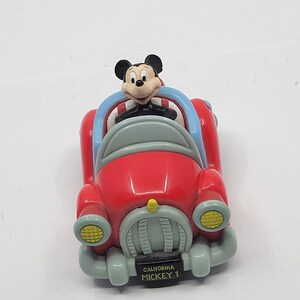 Puede incluir: Coche de juguete rojo con una figura de Mickey Mouse conduciendo. El coche tiene un interior azul y blanco y una placa de matr&iacute;cula que dice "California Mickey 1".