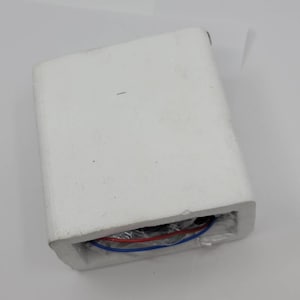 May include: A white rectangular foam block with a recessed area containing red and blue wires. The wires are visible through a clear plastic covering. The foam block is on a white surface.