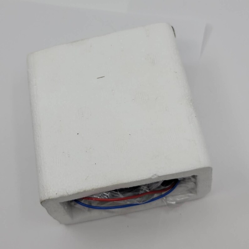 May include: A white rectangular foam block with a recessed area containing red and blue wires. The wires are visible through a clear plastic covering. The foam block is on a white surface.