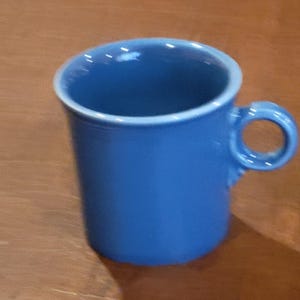 May include: A solid blue ceramic mug with a smooth, glossy finish and a circular handle. The mug features a slightly flared rim and a cylindrical body, showcasing a vibrant, uniform blue colour throughout the entire exterior and interior surface.