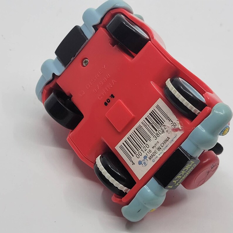 Puede incluir: Coche de juguete rojo con un dise&ntilde;o de Mickey Mouse azul y blanco. El coche tiene ruedas negras y una pegatina en la parte inferior que dice "Disney 97988 China 00120 38052 3 116 M919 Made in China The Walt Disney Company Mickey 1 California"