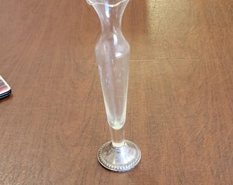 May include: A clear glass bud vase with a ruffled top and a silver base. The vase is etched with a pattern of lines.