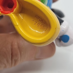 May include: Yellow plastic toy featuring a black and white Mickey Mouse design. The underside of the toy has the text "2001-1 29063" printed on it.