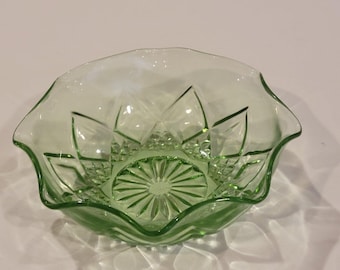 Puede incluir: Un cuenco de cristal verde claro con borde festoneado y un patrón geométrico prensado. La base interior muestra un diseño de rayos de sol, mientras que los lados están decorados con facetas en forma de diamante y texturas.