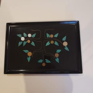 May include: A rectangular black tray featuring a central tree design with thin white lines for branches. The tree is decorated with small, textured teal leaf inlays and several circular metallic coins embedded as fruit.