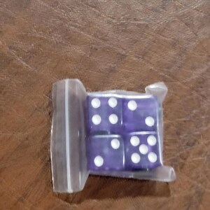 Puede incluir: Cuatro dados morados con puntos blancos están empaquetados en una bolsa de plástico transparente. Los dados son de color morado translúcido y los puntos están espaciados uniformemente. Los dados probablemente se utilizan para juegos de mesa u otros juegos de azar.