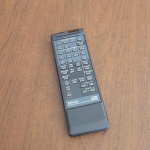 Puede incluir: Un mando a distancia rectangular negro Denon RC-230 para reproductor de discos compactos. El dispositivo cuenta con numerosos botones rectangulares grises para la selección de pistas, controles de reproducción, volumen y gestión de discos.