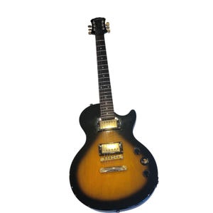 Puede incluir: Una guitarra eléctrica negra y marrón con herrajes dorados. La guitarra tiene un acabado sunburst, que va del negro al marrón y al amarillo. La guitarra tiene un clavijero negro y un diapasón con incrustaciones blancas. Se ven dos perillas y un interruptor.