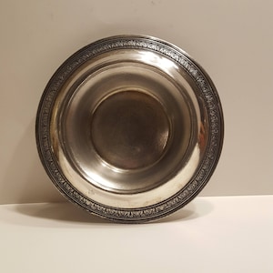 May include: A silver bowl with a decorative rim. The bowl is round and has a smooth, shiny surface.