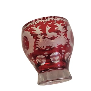 May include: A ruby red glass with etched white designs. The glass features a deer, foliage, and decorative patterns. The base is clear and faceted. This vintage glass is ideal for serving beverages.